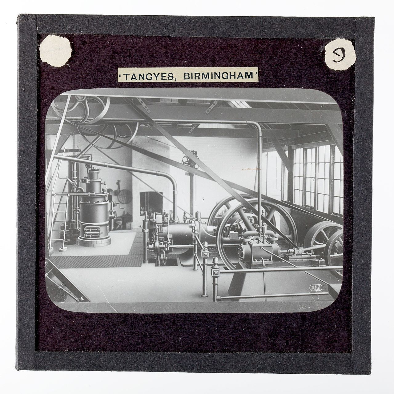 A Tangyes suction-gas producer plant and gas engine of about 1910: a tall cylindrical gas producer at left, the engine and generating set driven by belts from large flywheels at right. A lantern slide captioned 'Tangyes, Birmingham'.