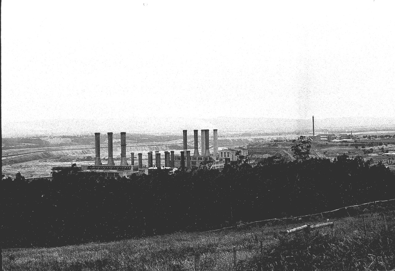 The Yallourn power station: a long powerhouse building bristling with chimney stacks, seen across the bush of the Latrobe Valley.